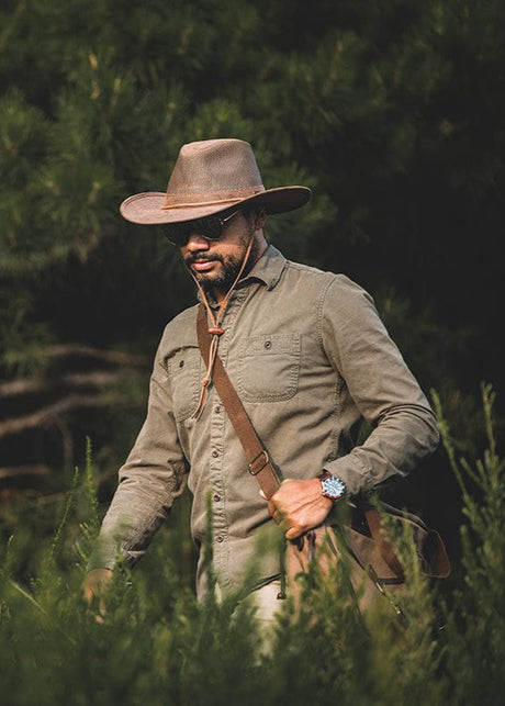 Man in brown hat and beige shirt walking through greenery